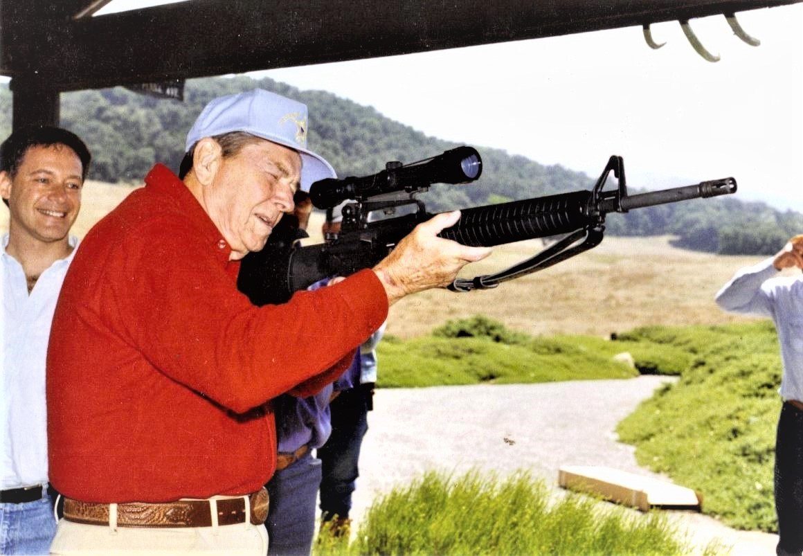 A man holding a rifle while standing next to another man.